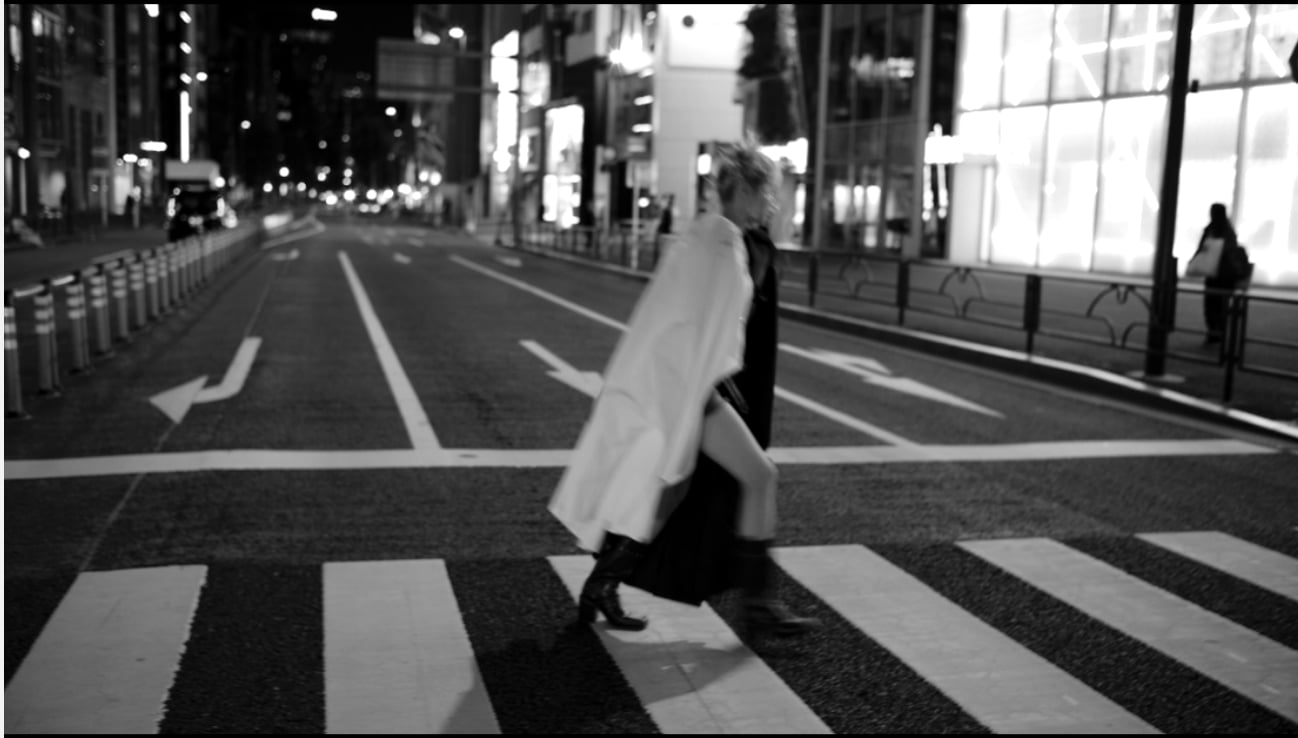 夜の原宿の交差点を、ハイトーンの髪で歩く人物。iLe のデザインカラー。